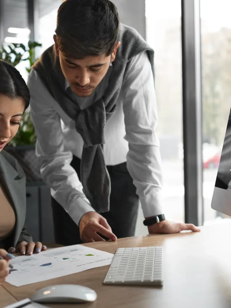 Two colleagues at a desk reviewing a report on a monitor