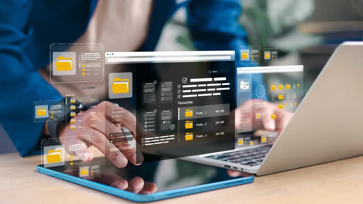 Hands on a tablet and laptop, with floating panels of yellow file folders