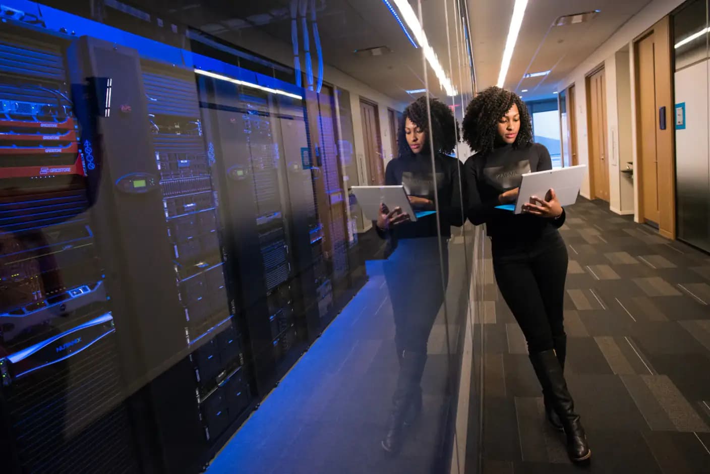 An engineer with a tablet walking beside a row of server racks.
