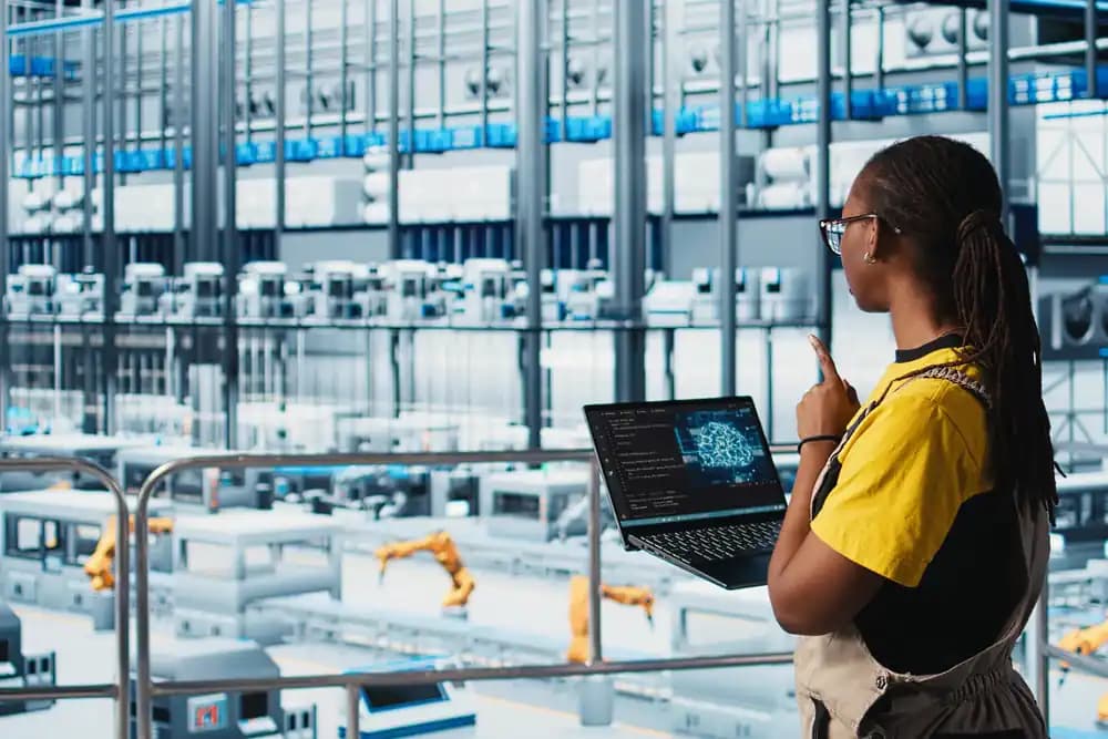 An engineer with a laptop beside a line of robot arms